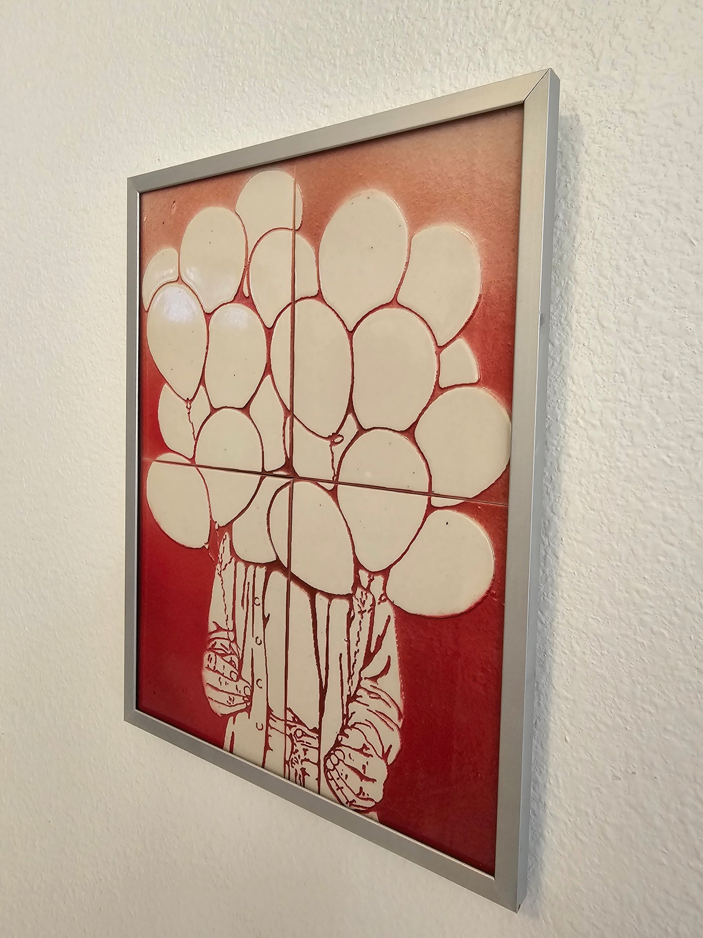 This is aside view of a mural of 4 handmade tiles showing an imaginary image of a person offering a bundle of balloons. These tiles are glued to a waterproof backing board with an aluminum frame.
These tiles are handmade porcelain ceramic tiles that could be installed as kitchen wall tiles, kitchen backsplash tiles. 
This image is intended to remind us of our connection to nature.