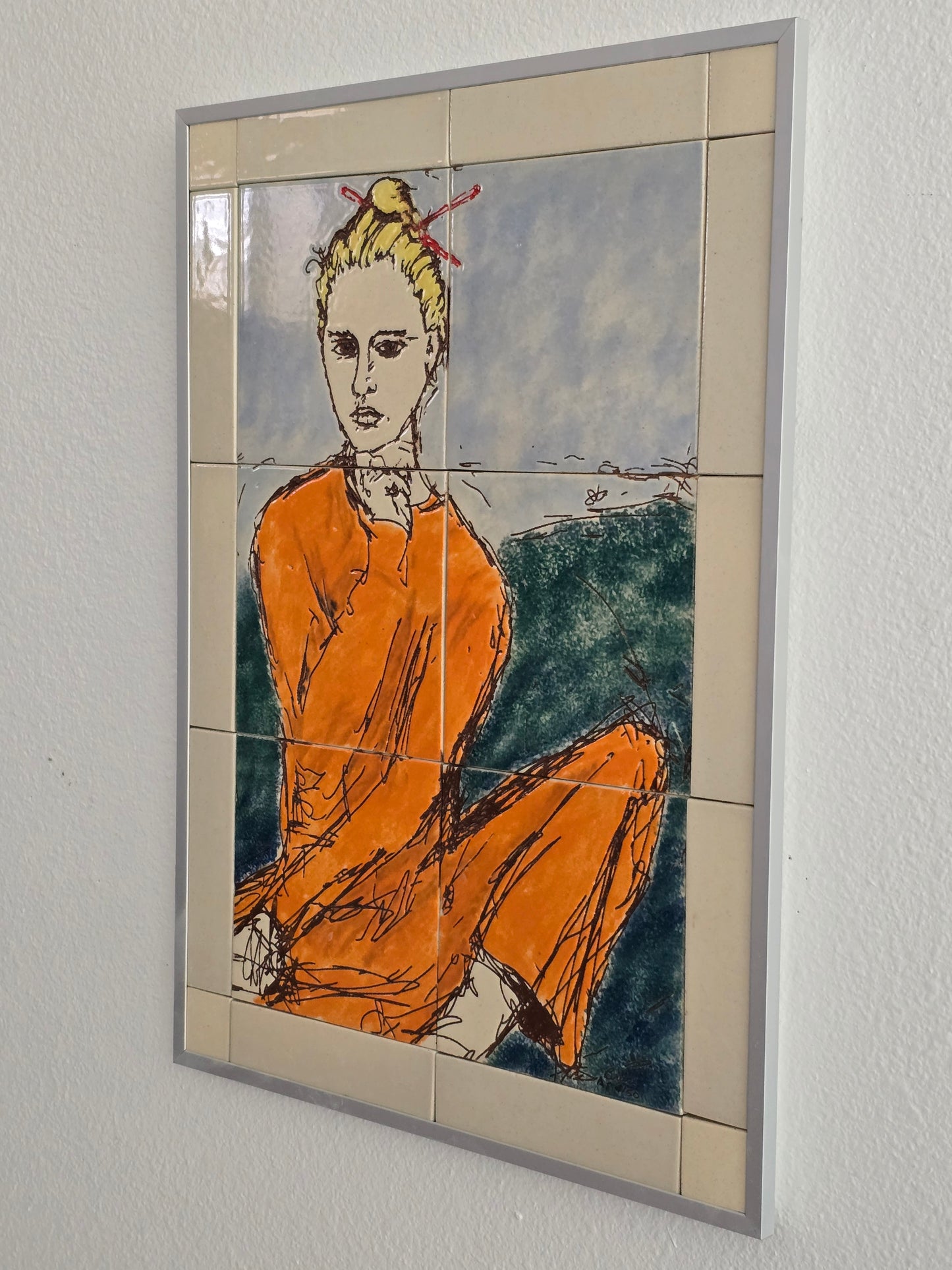 This is a side view of a set of 20 mounted and framed tiles depicting a woman with chopsticks. The woman is dressed in an orange sweatshirt and pants with a green and blue background. 